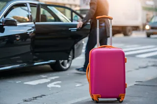 Resväska framför en taxi som någon sätter sig i